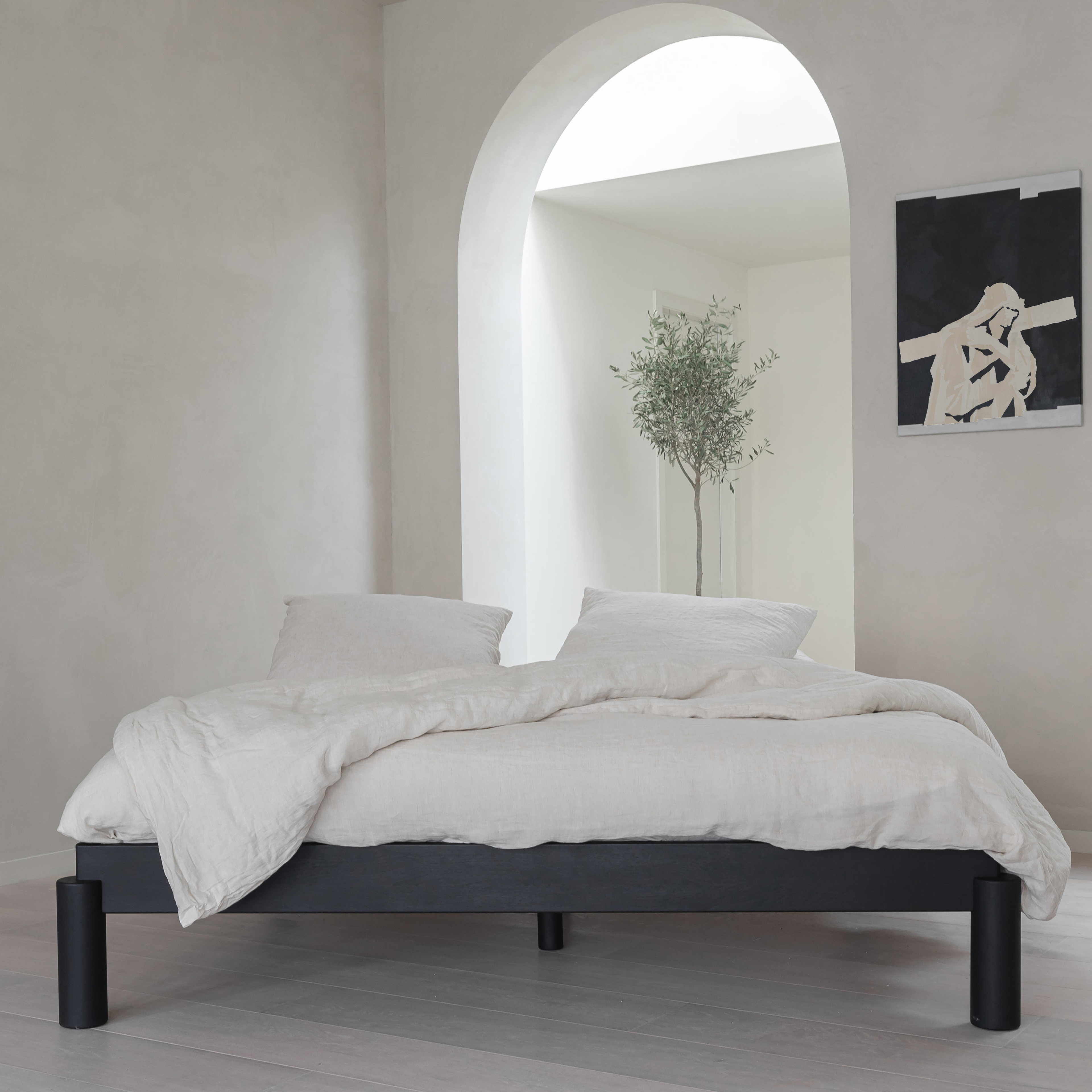 Minimalist black wood platform bed frame with white linen bedding and modern Jesus artwork on wall.