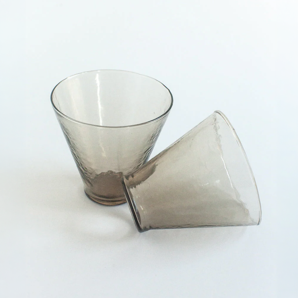Two smoky grey glass cups with tapered silhouette, designed for modern tableware collections.