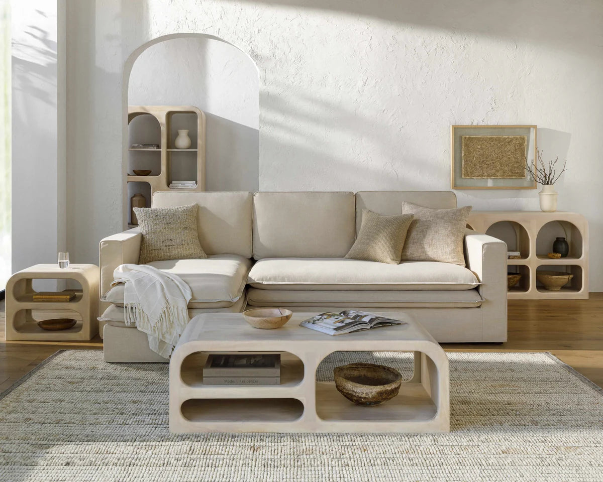 Beige sectional sofa in a modern living room with wooden coffee table and shelves.